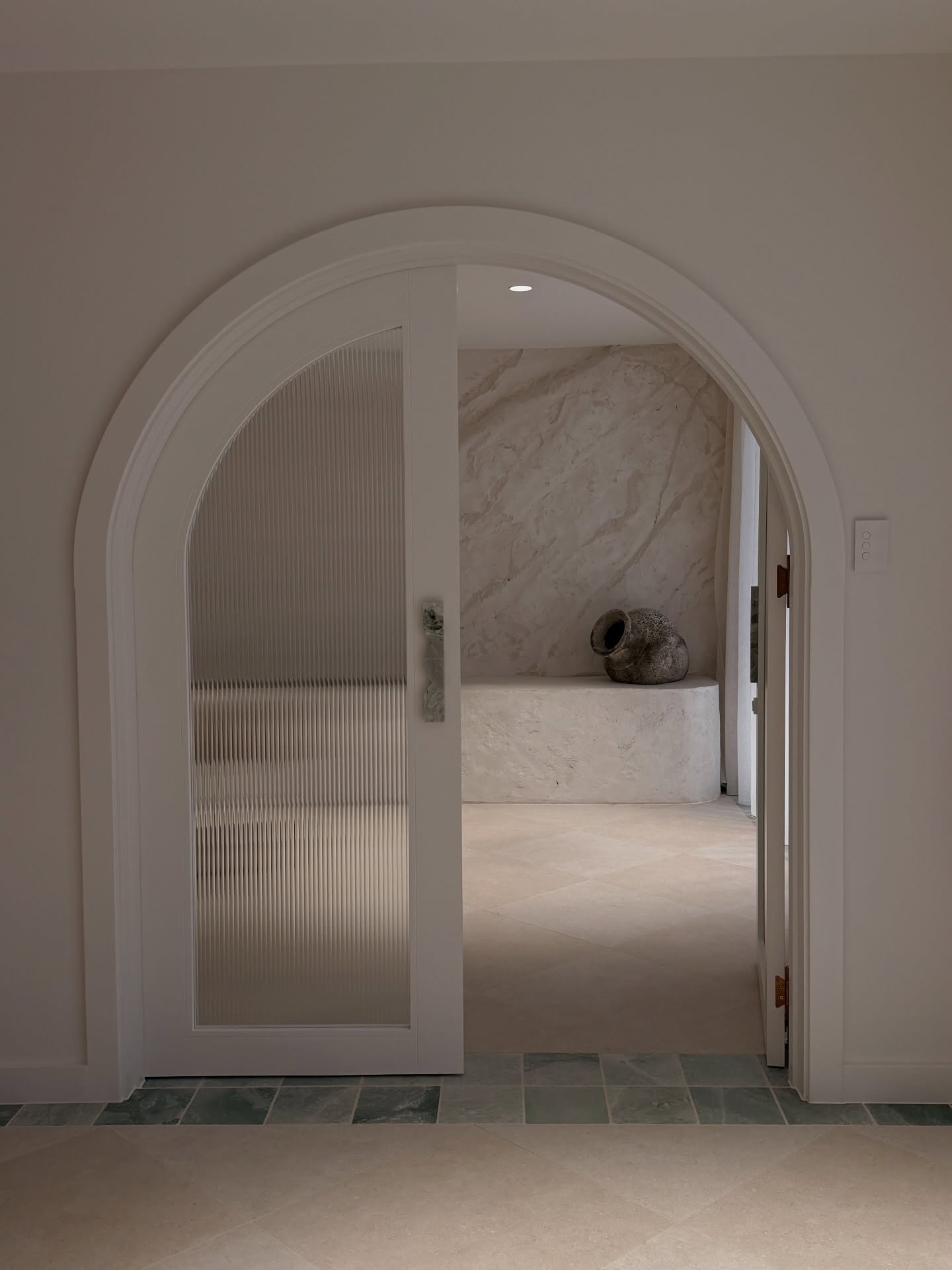 Arched doorway with fluted glass leading into a stone-finished clinic interior